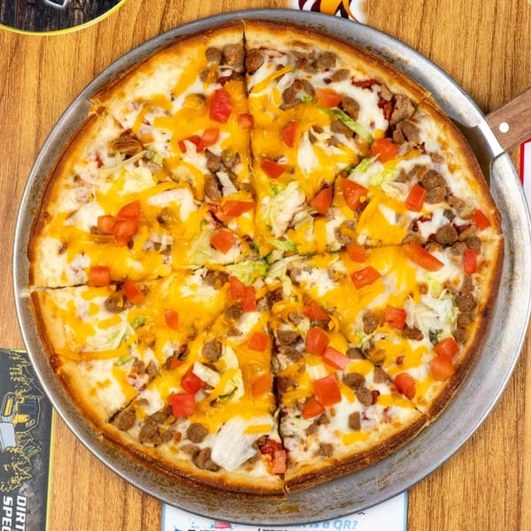 Overhead view of a taco pizza with ground beef, cheese, lettuce, and tomatoes on a wooden table.