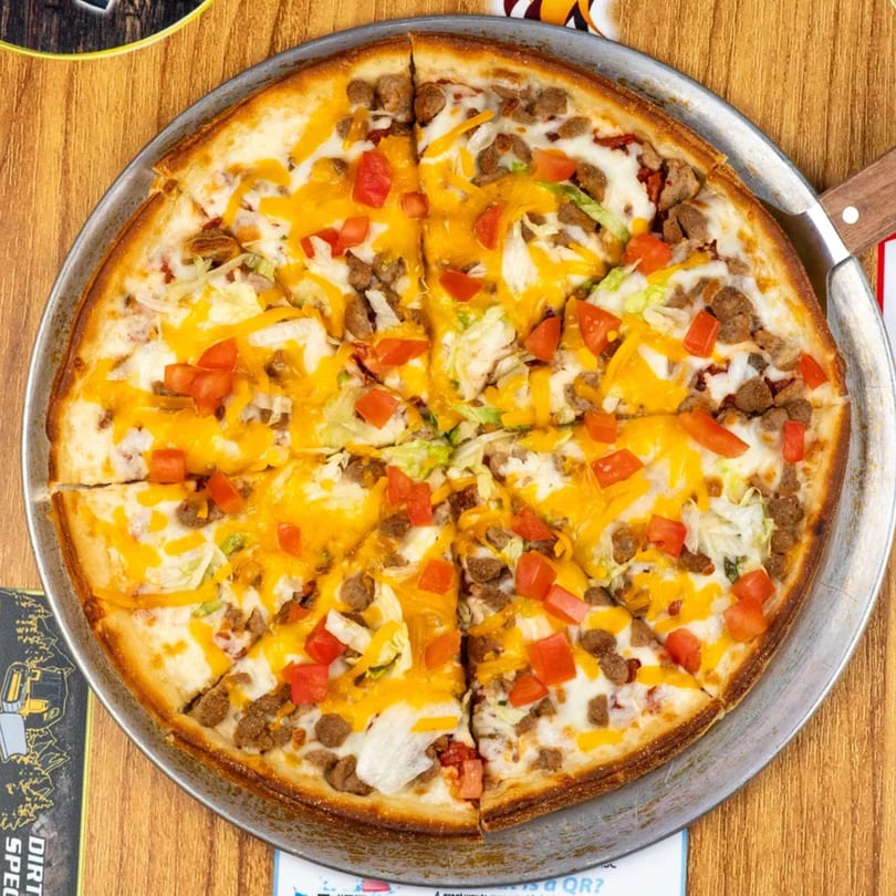 Overhead view of a taco pizza with ground beef, cheese, lettuce, and tomatoes on a wooden table.
