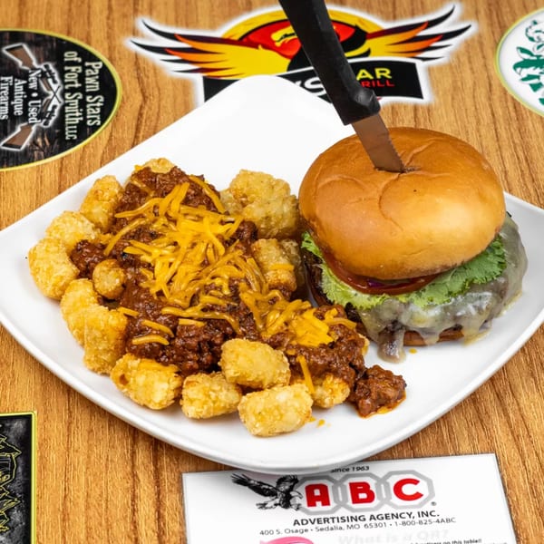 A burger with melted cheese and lettuce, next to chili cheese tater tots on a white plate.