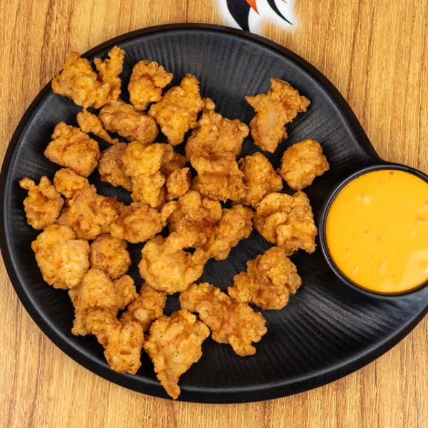 Crispy fried chicken bites on a black plate with a side of orange dipping sauce.
