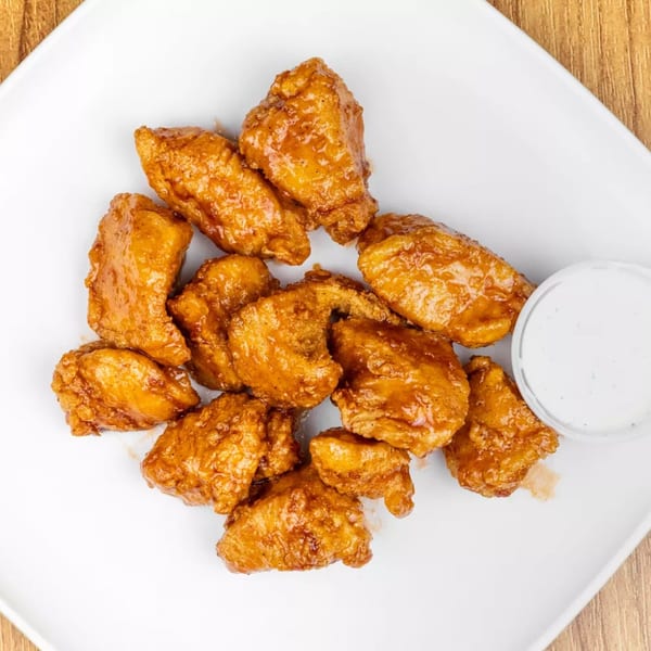A white plate holds a pile of golden-brown boneless chicken wings with a side of ranch.