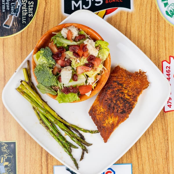 Blackened fish fillet with a side salad in a wooden bowl and grilled asparagus on a white plate.