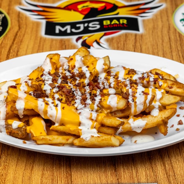 Loaded fries with melted cheese, ranch dressing, and bacon bits on a white plate.