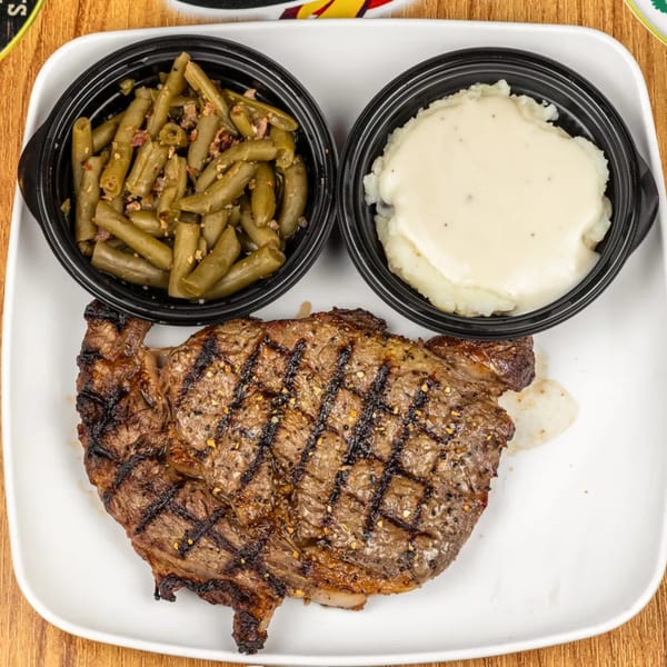 Grilled steak with grill marks, a side of green beans, and mashed potatoes with gravy.