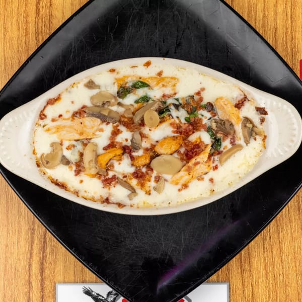 Creamy baked dish with chicken, mushrooms, spinach, and bacon bits in a white oval dish.